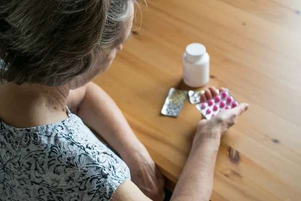 Hasta, yaşlı bir kadın evde, masanın yanına oturur ve haplara bakar.