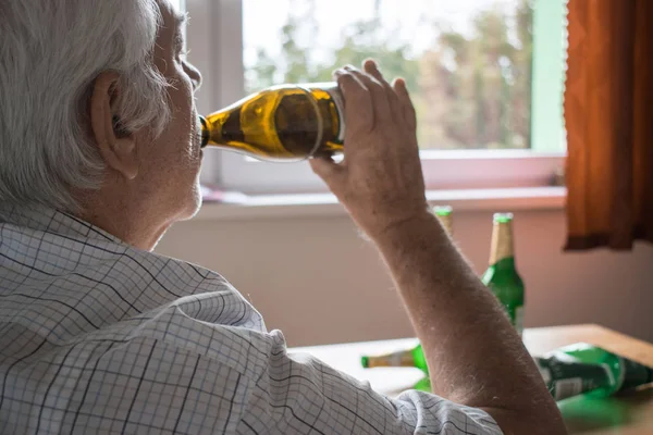 Viejo senior hombre sentarse al lado de mesa beber alcohol botella en casa triste — Foto de Stock