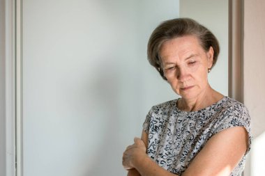 Üzgün yaşlı kadın evde tek başına depresif bir şekilde dikiliyor. 