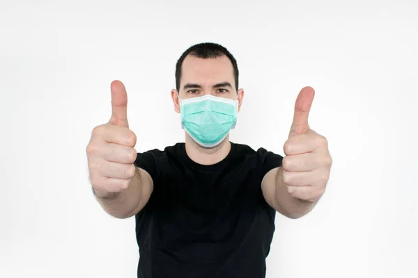 Erkek, genç, siyah tişört yüzünde beyaz arka plan maskesi duruyor. İki elinle kendini koru.