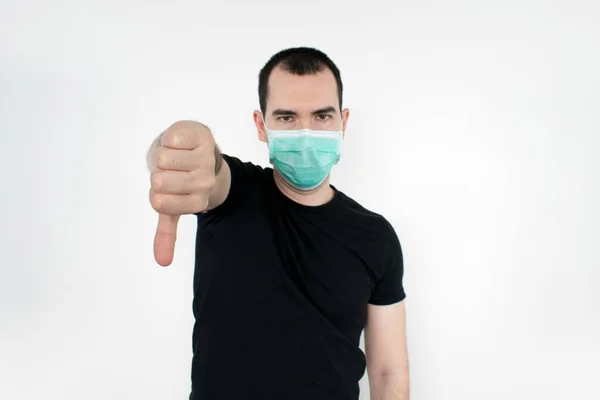 Erkek, genç, siyah tişört beyaz arka plan maskesi takıyor. Bir el Coronavirus sembolü. İstemem. reddetme 