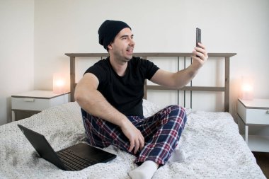  Ana konu odaklanamıyor ya da odaklanamıyor. Genç erkek, evde oturup içerik yaratıyor. Akıllı telefon dizüstü bilgisayarını tut ve gülümse.