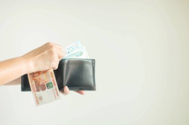 Hand holding a wallet and Russian money in RUB currency; another hand-selecting more banknotes from the wallet prepare for spending on white background with copy space, select focus at the right hand.