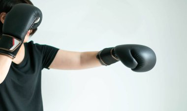 Close-up side view of a woman in a black T-shirt and black boxing gloves stretching her left fist forward or called left jab; and use right fist guarding on white background; selected focus at the tip of two fists.