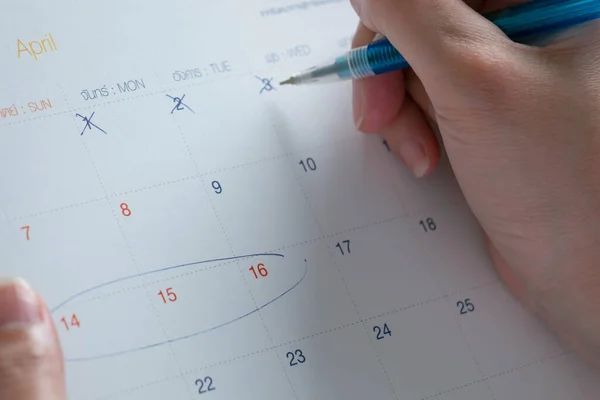Close-up of a hand holding a pen cross out at date in April in Thai calendar, for counting down to planned traveling at day-off in Songkran festival. (in Thai calendar have the Thai language that meaning the day in a week)