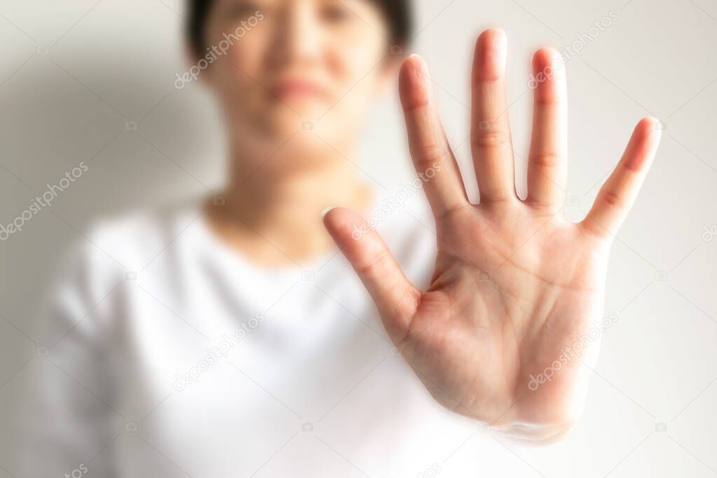 A woman raises an arm and showing a palm with five fingers; it is hand signs or the body language in the meaning of please stop; say no; or forbid, on a white background and selected focus only at the palm.