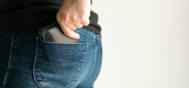 Yan planda ve yakın planda bir kadının sol elini kot pantolonunun arka cebindeki mavi deri para cüzdanını kullanarak ödemesi için para çıkarması; finansal ve ticari kavramlar.