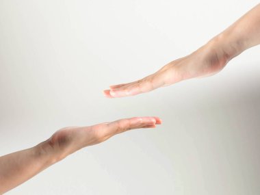 Beyaz arka planda neredeyse birbirine dokunan iki kişinin eli; normal durumda sevgi ve bakım ifade etmek için çok iyidir; ama bulaşıcı hastalık durumunda bu bir önlem. Sosyal uzaklık, sağlık ve tıbbi bakım kavramı.