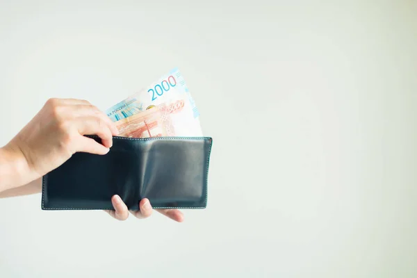 Kısa bir cüzdan tutan ellerin yakın çekimi ve diğer bir el Ruble veya RuB para birimini ortaya çıkarır; beyaz arka planda bir şey ödemek için cüzdan. Banknotlarda seçili odak.