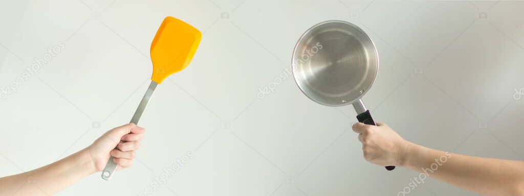Hands of two persons that holding the spatula against the pot ready for cooking; a symbol of chef and meal; concept of fry and stir fry that has fat versus the boil and stewed food that low calories.