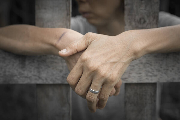 prisoner hands behind wooden bars : criminal locked in jail waiting for release - selective focus used