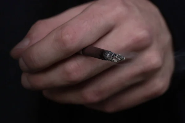 Smoldering cigarette in hand on a dark background — Stock Photo, Image