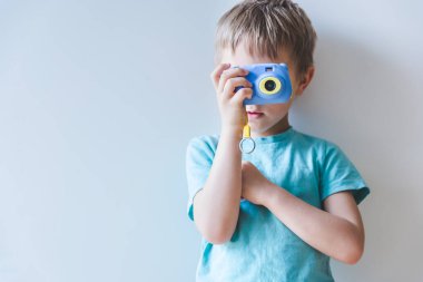 Elinde kamerayla evde fotoğraf çeken sarışın küçük bir çocuk.