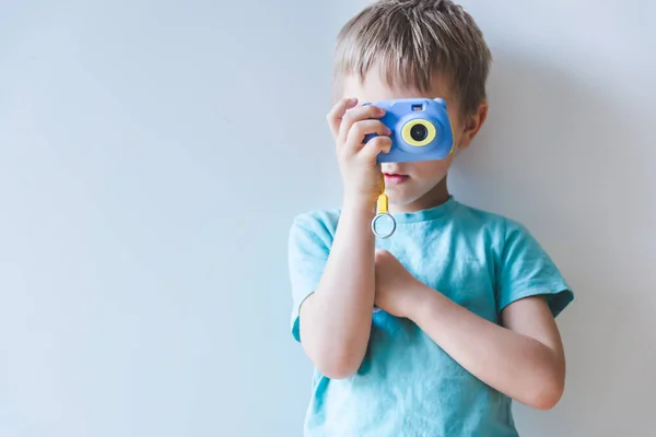 Elinde kamerayla evde fotoğraf çeken sarışın küçük bir çocuk.
