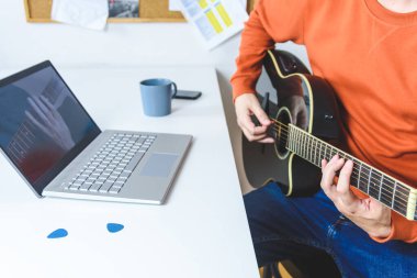 Beyaz adam video dersleriyle akustik gitar çalmayı öğreniyor.