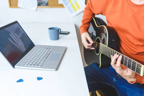 Beyaz adam video dersleriyle akustik gitar çalmayı öğreniyor.