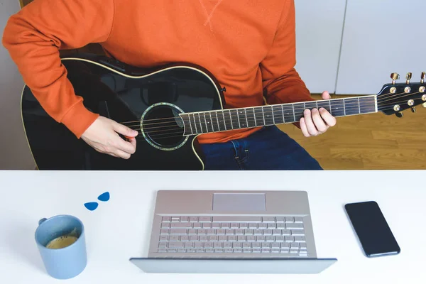 Beyaz adam bilgisayarla akustik gitar dersleri alıyor.