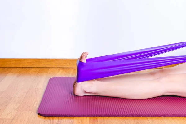 Beyaz bir kadının mor bir spor bandıyla buzağılarını esnettiğinin ayrıntıları.