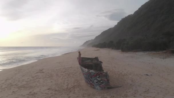 日落时分 女孩坐在沙滩上的一艘船的残骸上 — 图库视频影像