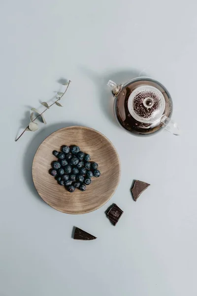 Uma placa de madeira com mirtilos em uma mesa ao lado de um bule de chá de vidro — Fotografia de Stock