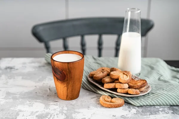 Ένα ξύλινο ποτήρι με γάλα στο τραπέζι της κουζίνας κοντά στα μπισκότα — Φωτογραφία Αρχείου