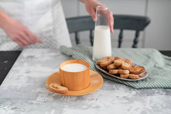 Önlük giymiş bir kadının elleri şişeden çıkan bir bardağa süt döktü.
