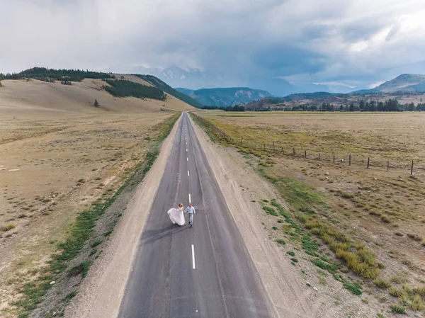 Gelinlik giymiş gelin ve damat yol boyunca yürüyor.