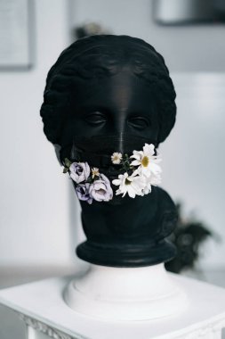 Siyah sıva bir kadın heykeli. Siyah bir tıbbi maske ve taze çiçekler.
