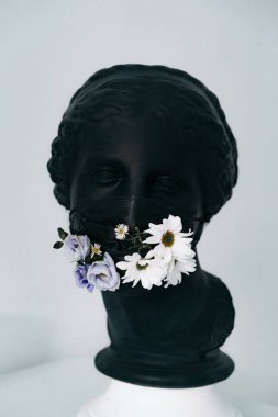 Siyah sıva bir kadın heykeli. Siyah bir tıbbi maske ve taze çiçekler.