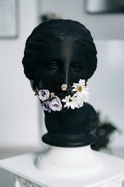 Siyah sıva bir kadın heykeli. Siyah bir tıbbi maske ve taze çiçekler.