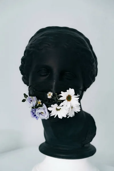 Siyah sıva bir kadın heykeli. Siyah bir tıbbi maske ve taze çiçekler.