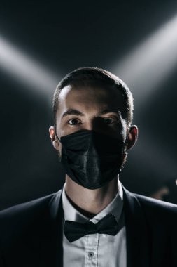 Siyah takım elbiseli damadın yüzü ve siyah arka planda siyah bir tıbbi maske.