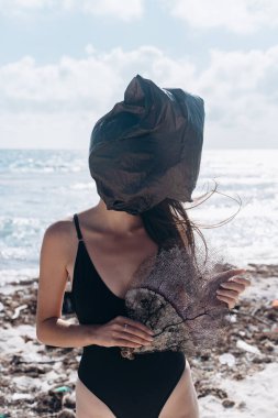 Kafasında plastik torbayla siyah mayo giymiş bir kız ve Karayipler 'deki dağınık bir sahilde ölü bir ağılla.