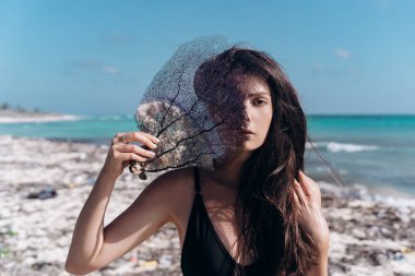 Siyah mayo giymiş bir kız, Karayipler 'in kumlu kumlu sahillerinde ölü mercanı yüzüne tutuyor.