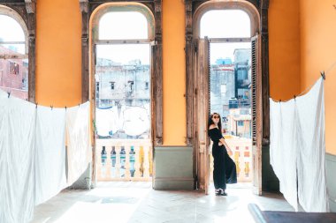 Siyah tulumlu bir kız eski bir İspanyol tarzı koloni evinin balkonunun çıkışında duruyor.