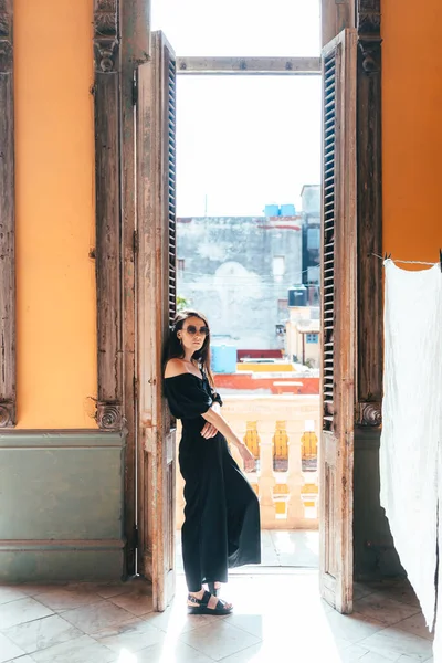 Siyah tulumlu bir kız eski bir İspanyol tarzı koloni evinin balkonunun çıkışında duruyor.