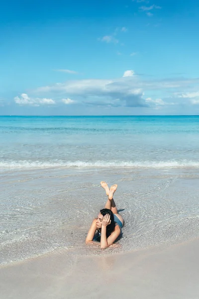 Girl lies in blue water on the sandy beach of the Caribbean