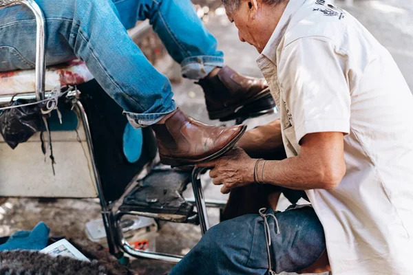 A man cleans shoes for a man sitting in front of him in an armchair in the center of Mexico City