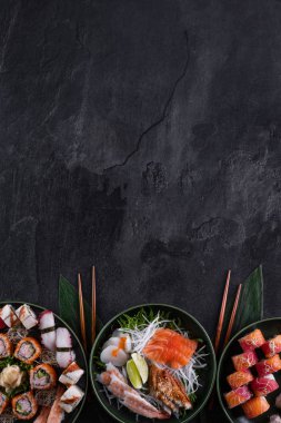 Koyu arkaplanda çeşitli suşiler var. Somon, istiridye, yılan balığı ve karidesli saşimi ile daikon turplu suşi. Uzayı metin için kopyala. Restoran menüsü. Geleneksel Japon yemekleri..