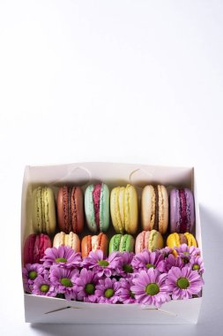 Beyaz arka planda hediye kutusunda çiçekli renkli badem kurabiyeleri. Sevgililer Günü (14 Şubat), Anneler Günü, Doğum günü veya Kadınlar Günü (8 Mart) konsepti. Fransız bademli bademli kurabiyeler. Boşluğu kopyala