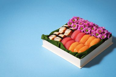 Suşi seti, parlak mavi arka planda hediye kutusunda çiçekler. Yaratıcı çikolata kutusu gibi. Sevgililer Günü (14 Şubat), Anneler Günü, Doğum günü, Kadınlar Günü (8 Mart) veya bahar konsepti. Boşluğu kopyala