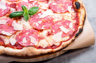 Gri taşlı arka planda tahta üzerinde pizza. İtalyan geleneksel yemekleri. Parmigiano-reggiano peynirli, sucuklu ve fesleğenli lezzetli pizza. Restoran menüsü. Boşluğu kopyala, üst görünüm
