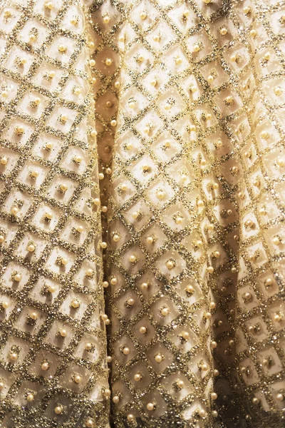 Wedding dress fabric texture background. Golden and ivory silk dress with beads, pearls, sparkles and embroidery. Vintage wedding dress detail. Elegant geometric pattern on fabric. Vertical, close up