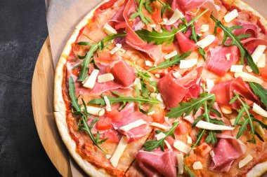Siyah taşlı arka planda tahta üzerinde pizza. İtalyan geleneksel yemekleri. Serrano jamon, parmigiano-reggiano peyniri ve roka ile nefis pizza. Restoran menüsü. Boşluğu kopyala, üst görünüm