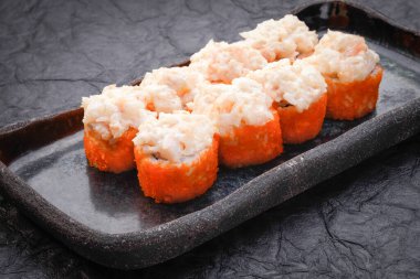 Suşi seti koyu arka planda servis edilir. Fırında makarna, masago, somon, krem peynir, avokado ve karidesli Philadelphia maki. Çeşitli suşiler. Japon yemeği. Restoran menüsü. Yan görünüm, kapat