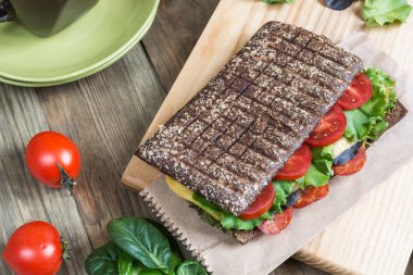 Panini - kahverengi ekmekli sandviç, domates, salata ve sosis ahşap arka planda..