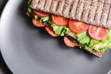 Sandviç, kahverengi ekmek, domates, marul, sosis, mozzarella ve siyah arka planda bir fincan kahve. Üst görünüm