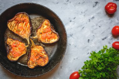 Siyah tavada ızgara patlıcan ya da kırmızı soslu fırın örtüsü maydanoz, gri arka planda domates. Menü tasarımı için metin alanını kopyala. Yatay üst görünüm. Sağlıklı vejetaryen atıştırmalıkları konsepti.