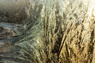 Sabah güneşinde donmuş pencere, sıcak renklerde parıldıyor. Donmuş camda dondurucu bir şafak.