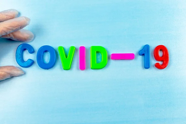 COVID-19 kelimesi çocukların çok renkli mektuplarından toplandı. Mavi arkaplandaki yazıt koronavirüsü..